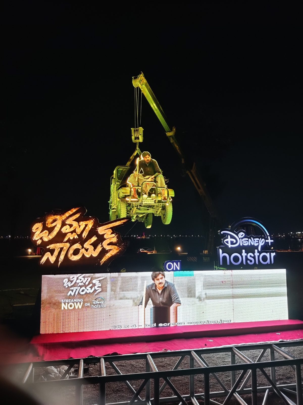 A jeep hung from a crane above a lit film promotion stage