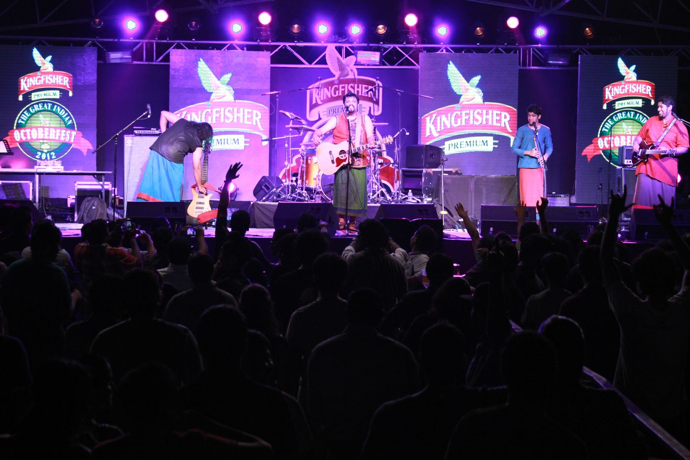 Band on a lit stage with the crowd raising their hands