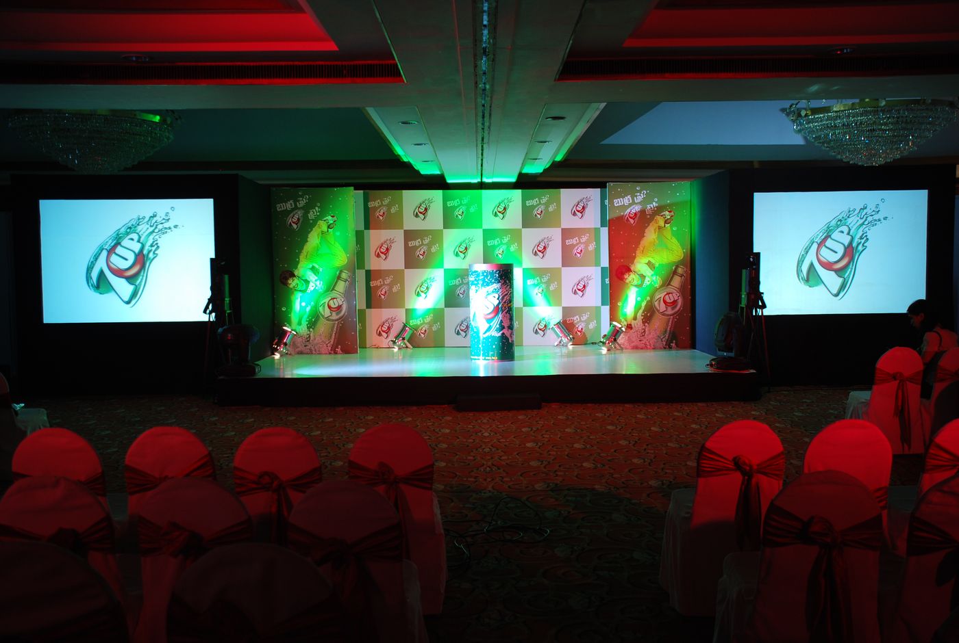Launch stage with two screens and green lighting over a seated hall